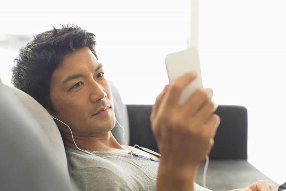 Man-listening-to-music-with-headphones-on-smart-phone-on-sofa Man listening to music with headphones